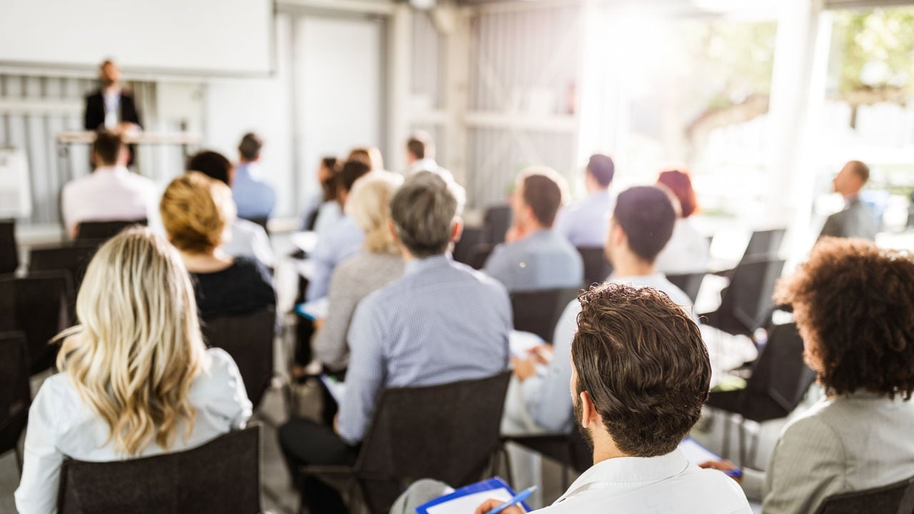 Rear view of large group of business people attending an education event in board room. Focus is on man in white shirt.