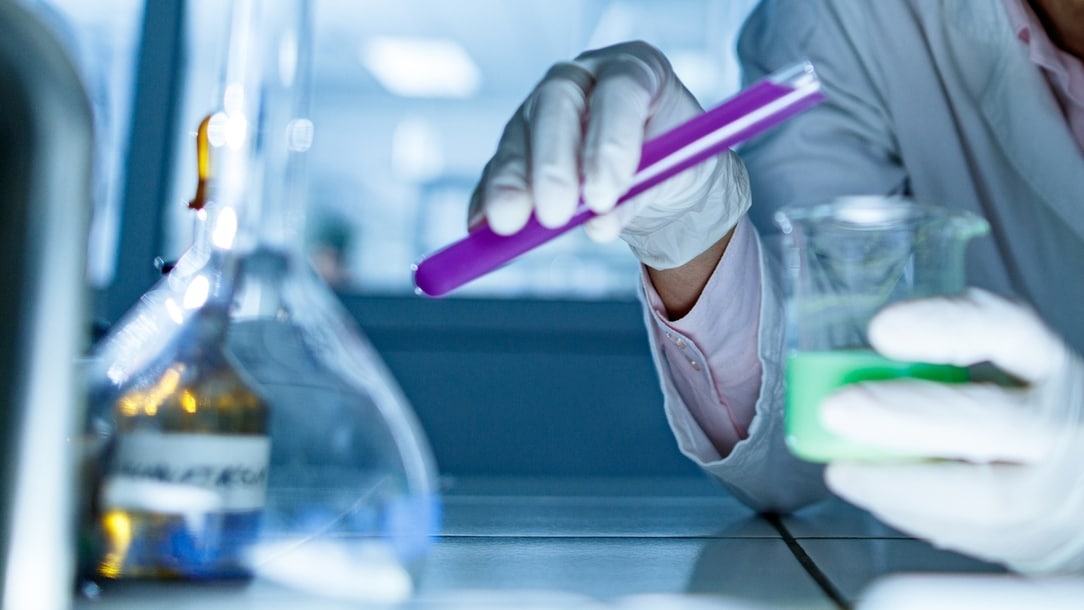 Mature female chemist mixing liquids from a test tube into a beaker while working in laboratory.