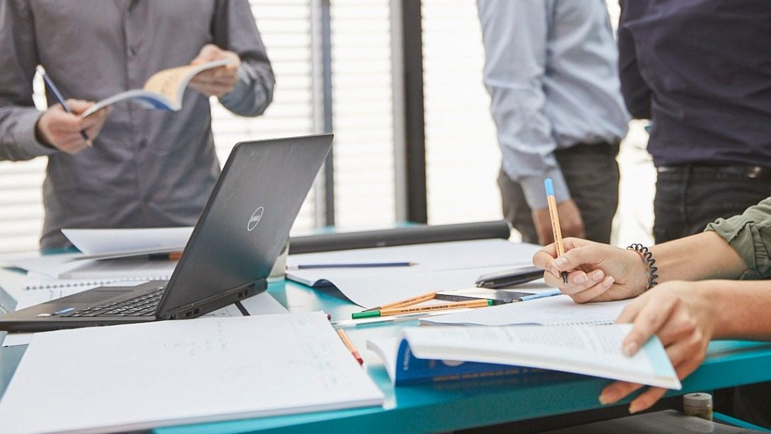 A group of people working together, surrounded by papers and laptop.